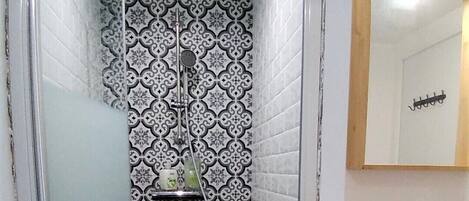 Une salle de bain avec des carreaux décorés, une douche, un lavabo et un miroir.