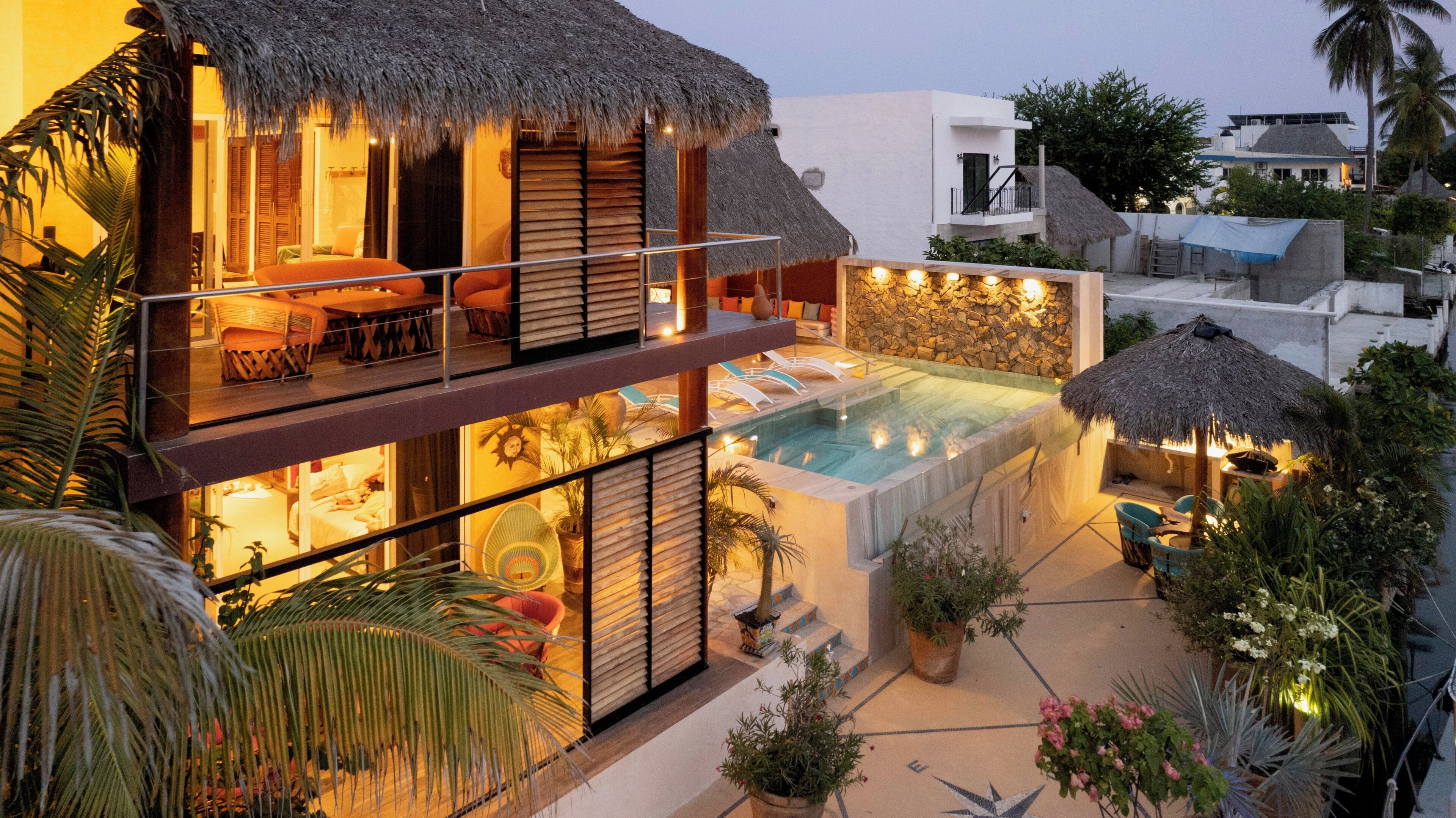 Un bâtiment à deux étages doté d’une piscine, d’un espace extérieur aménagé et de plantes tropicales.
