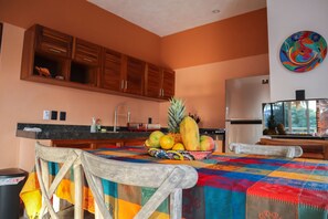 A kitchen with wooden cabinets, a fruit bowl on the counter, and a colorful tablecloth.