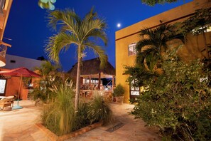An outdoor patio area with a thatched-roof structure, palm trees, and a stone floor.