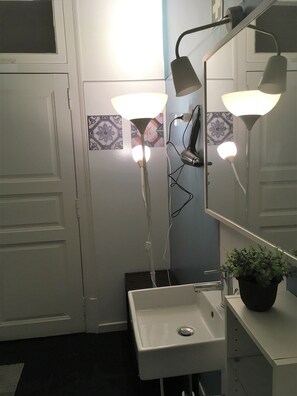 Een badkamer met een wit wastafelmeubel, twee wandlampen, een spiegel en een potplant op het aanrecht.