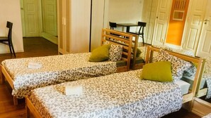 Une chambre avec deux lits simples, une tête de lit en bois, une petite table et une chaise.