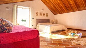 Een slaapkamer met een rood bed, een houten plafond en een stenen vloer.