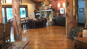 Een ruime woonkamer met een stenen openhaard, houten balken en een groot raam.