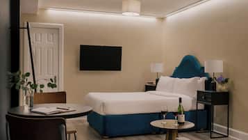 A hotel room with a bed, bedside tables, a TV, a desk with a chair, and a small table with a bottle and glasses.
