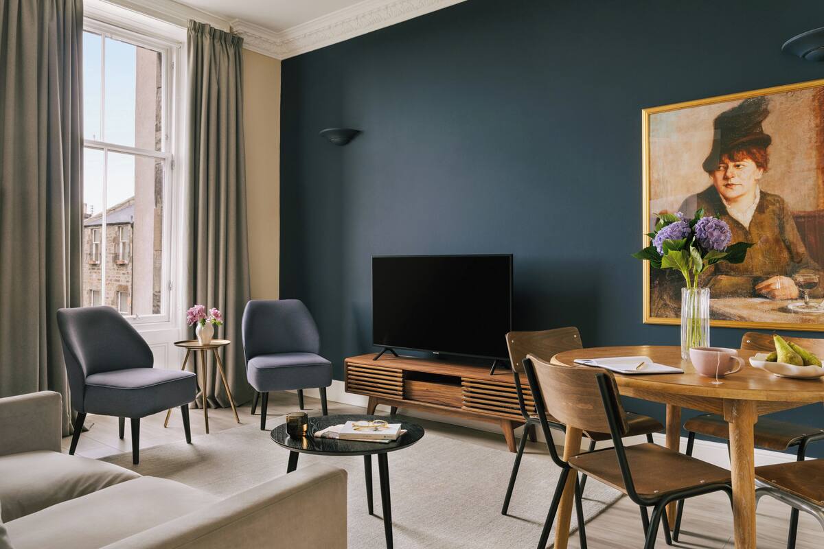 Una sala de estar moderna con televisor de pantalla plana, asientos cómodos, una mesa de comedor con sillas y un cuadro en la pared.