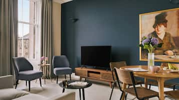 A modern living room with a flat-screen TV, comfortable seating, a dining table with chairs, and a painting on the wall.
