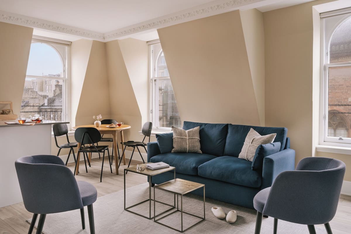 Una sala de estar moderna con un sofá azul, una mesa de centro y un comedor con sillas y una pequeña mesa.