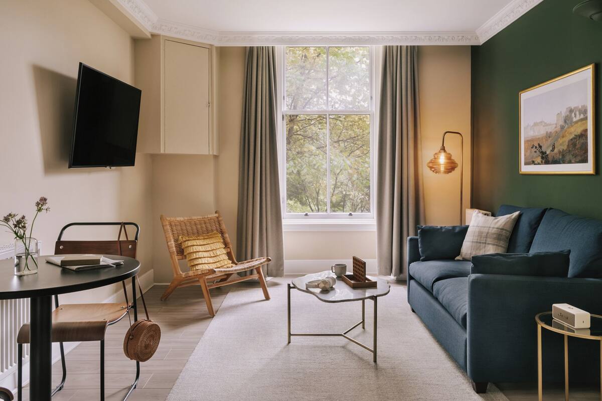 Una sala de estar con sofá, sillón, mesa de centro, televisor y ventana con cortinas.