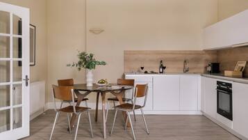 Een moderne keuken met witte kasten, een houten eettafel met vier stoelen, en een plant in een pot op de tafel.
