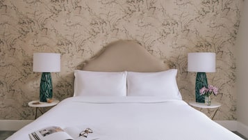A neatly made bed with white linens, two bedside tables with lamps, and a floral wallpaper pattern.