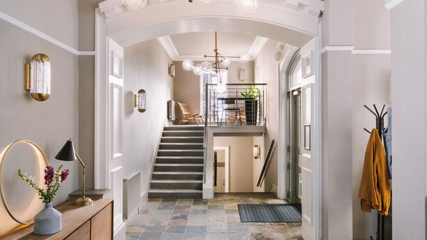 A grand staircase leading to a second floor, flanked by elegant wall sconces and a large mirror.
