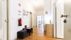 Un pasillo con suelo de madera, un extintor en la pared, un pequeño taburete negro y un tablón de anuncios con diversos avisos.