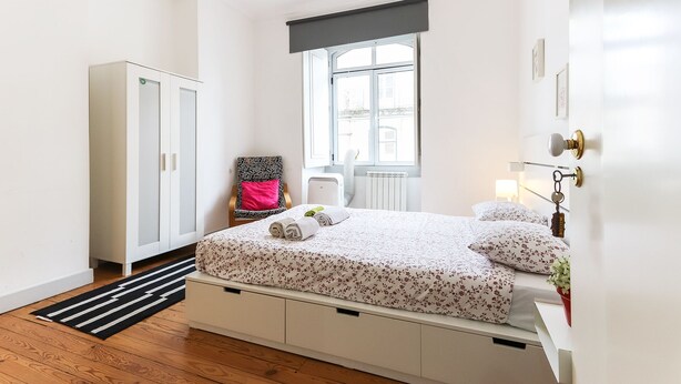 Un dormitorio con cama, armario, radiador, ventana y puerta.