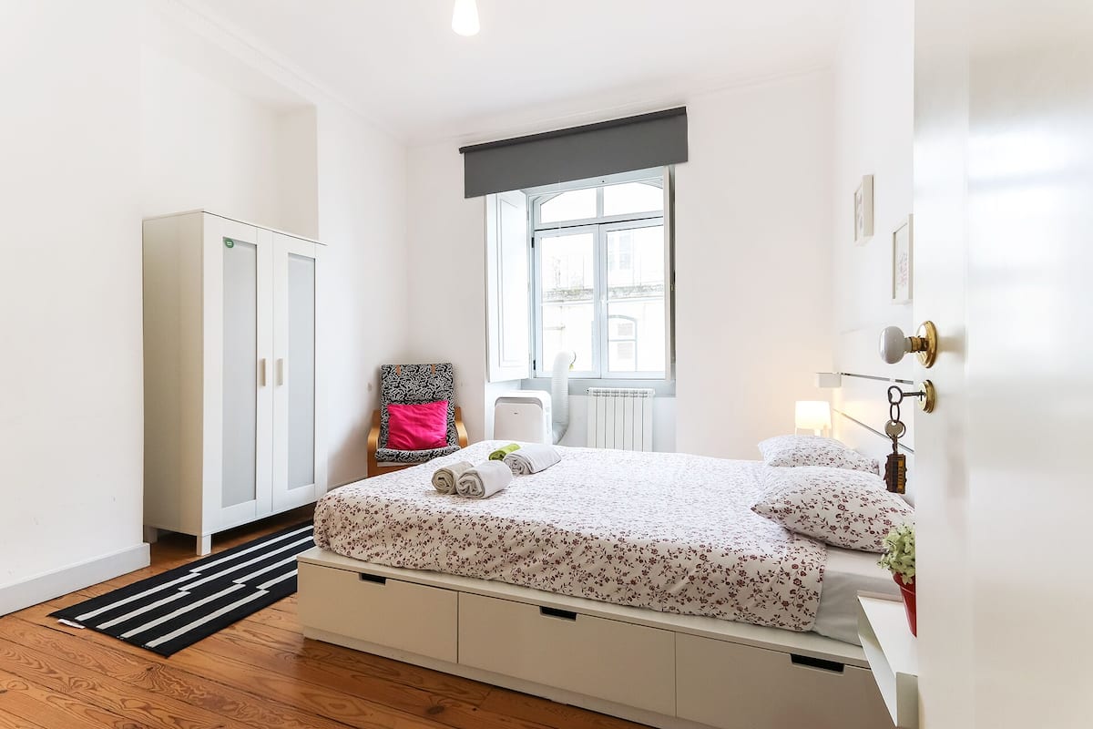 Quarto com cama, guarda-roupa, radiador, janela e porta.