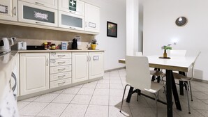 Una cocina con armarios blancos, una cafetera y un comedor con mesa y sillas.