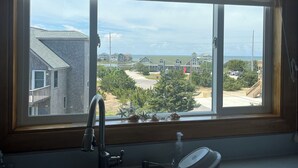 Eine Küche mit großem Fenster, einem Edelstahl-Spülbecken und Blick auf eine Wohngegend mit Häusern und Strand.
