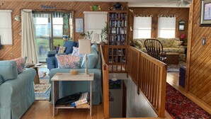 Ein gemütliches Wohnzimmer mit Holzboden, einer Bücherwand, einem blauen Sofa und einer Holztreppe.