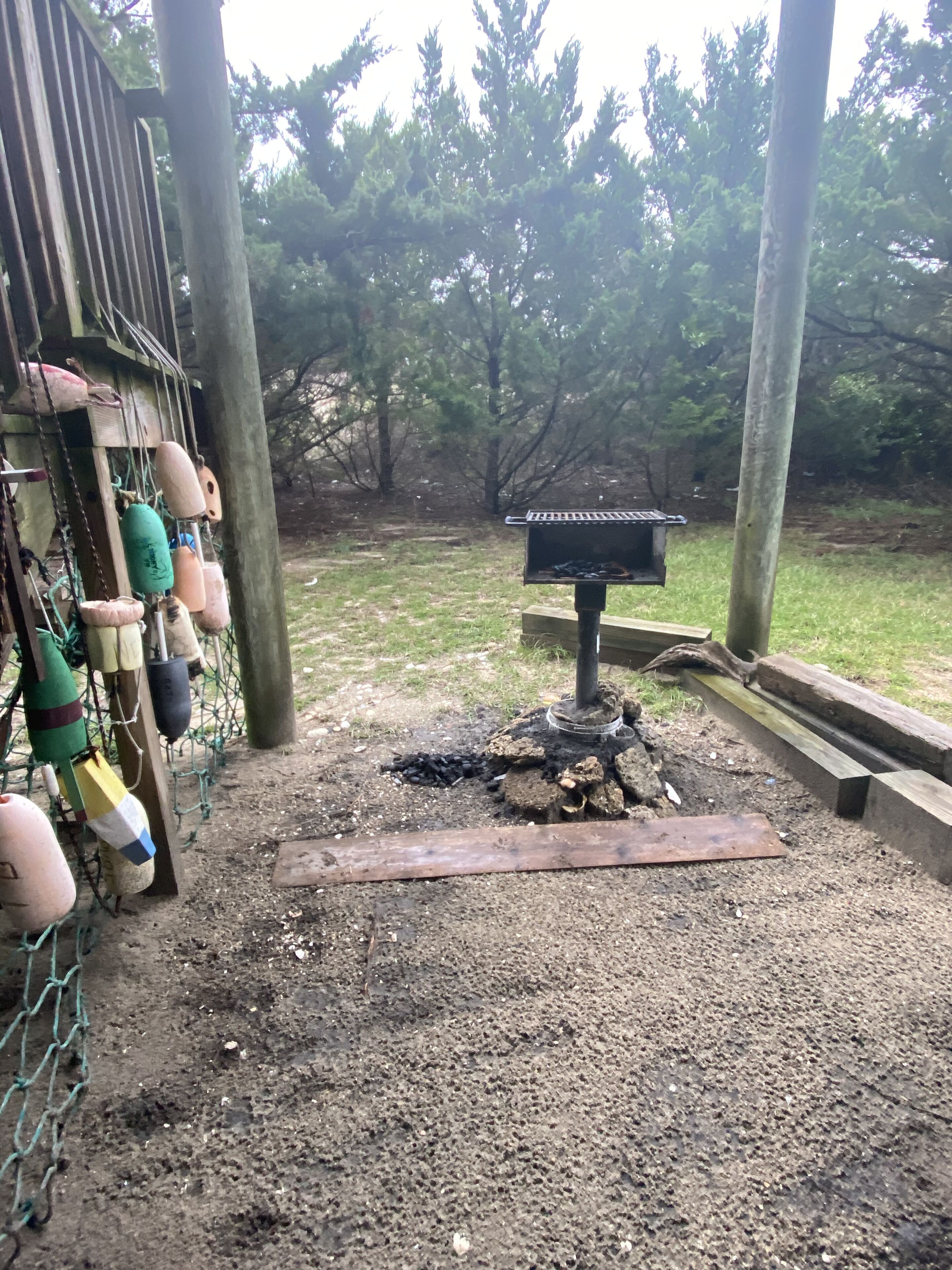 Un barbecue avec foyer intégré, entouré d’une clôture en treillis métallique et de poteaux en bois.