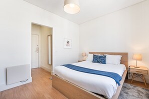 A hotel room with a bed, bedside tables, a lamp, a picture on the wall, and a door leading to another room. - GuestReady - Costa Cabral Guesthouse - Room 3 (Porto)