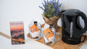 Une cafetière noire, deux tasses en verre avec des sachets de thé, une carte de la ville de Porto et un vase avec des fleurs bleues, le tout posé sur une planche en bois.