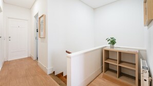 Un couloir avec une porte blanche, un tableau encadré au mur et une console en bois sur laquelle est posée une plante.