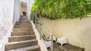 Un escalier avec des marches en pierre et une rampe en métal, menant à une pièce aux murs blancs et où une plante verte est suspendue au mur.