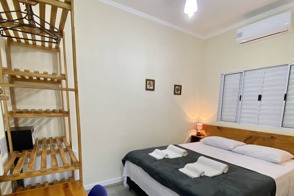 Una habitación de hotel con una cama, una estantería de madera, un escritorio y una mesita de noche.