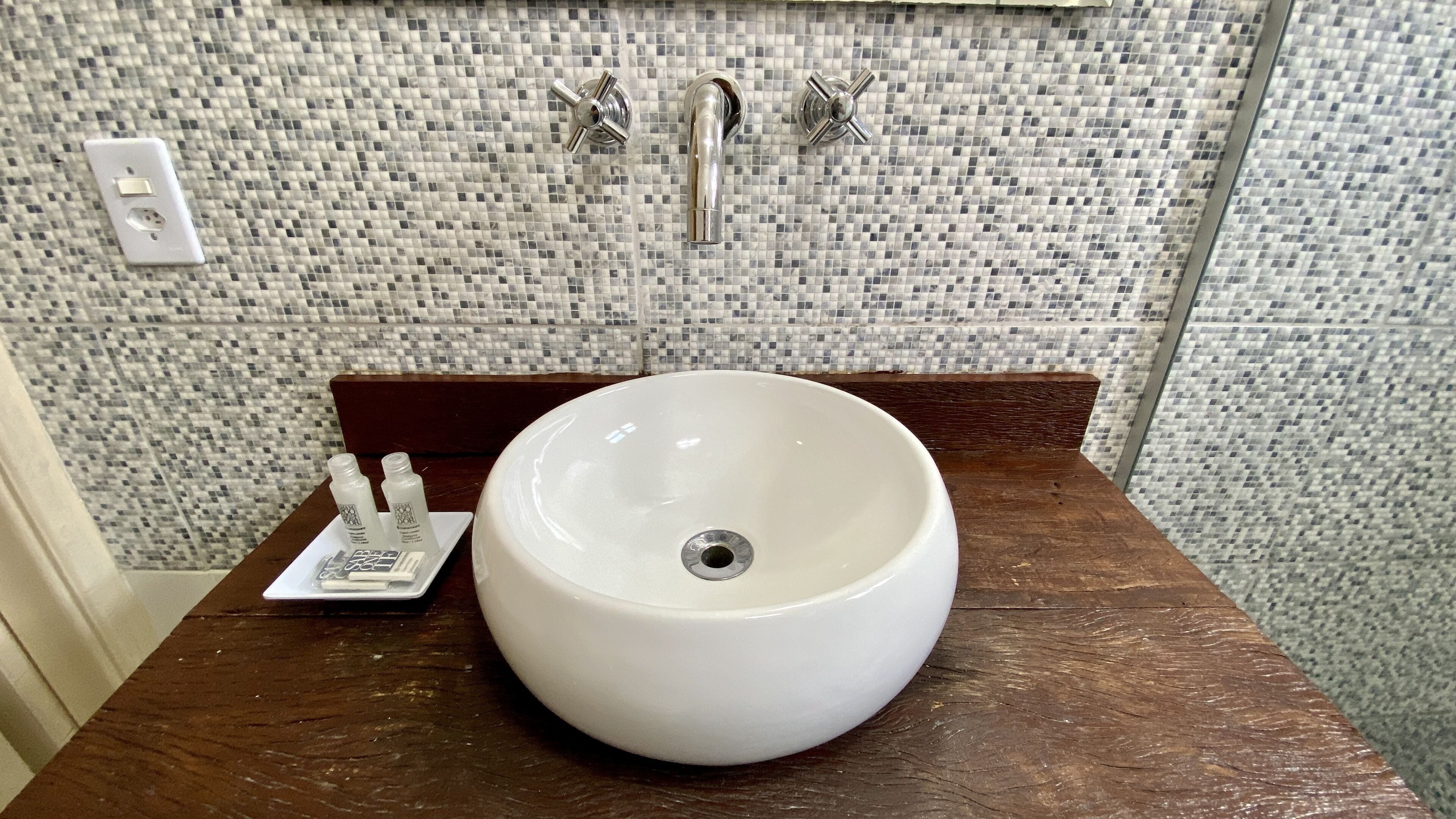 Un baño con un lavamanos blanco, un mueble de tocador de madera y un salpicadero de azulejos.