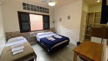 A room with two beds, a wooden table, a ceiling fan, and a window with blinds.