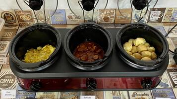 A buffet with three food stations: scrambled eggs, sausage, and potatoes.