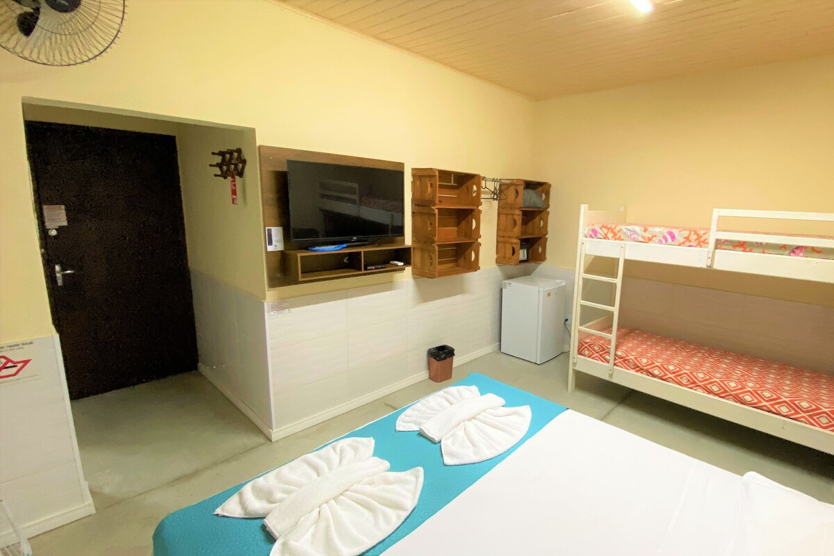 A room with bunk beds, a television, a small refrigerator, and a fan.