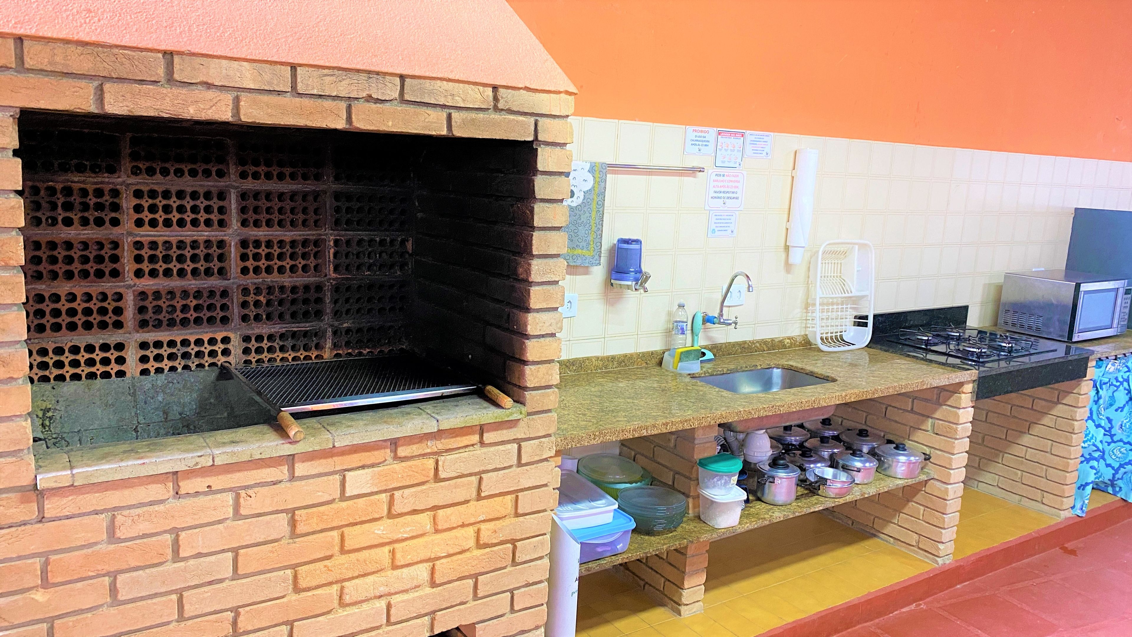 Uma cozinha com forno de tijolos, pia, fogão e diversos utensílios.