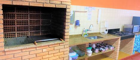 Uma cozinha com forno de tijolos, pia, fogão e diversos utensílios.