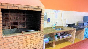 A kitchen with a brick oven, a sink, a stove, and various kitchen utensils. - Suíte Lázaro (Ubatuba)