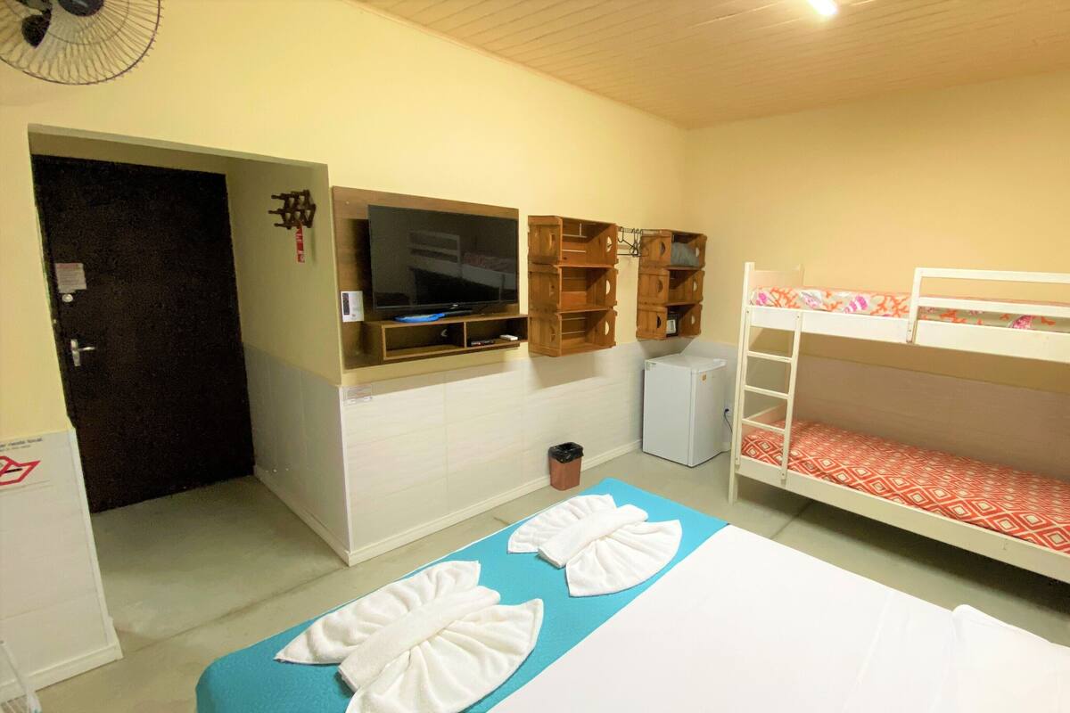 Una habitación con literas, televisión, un refrigerador pequeño y un ventilador.