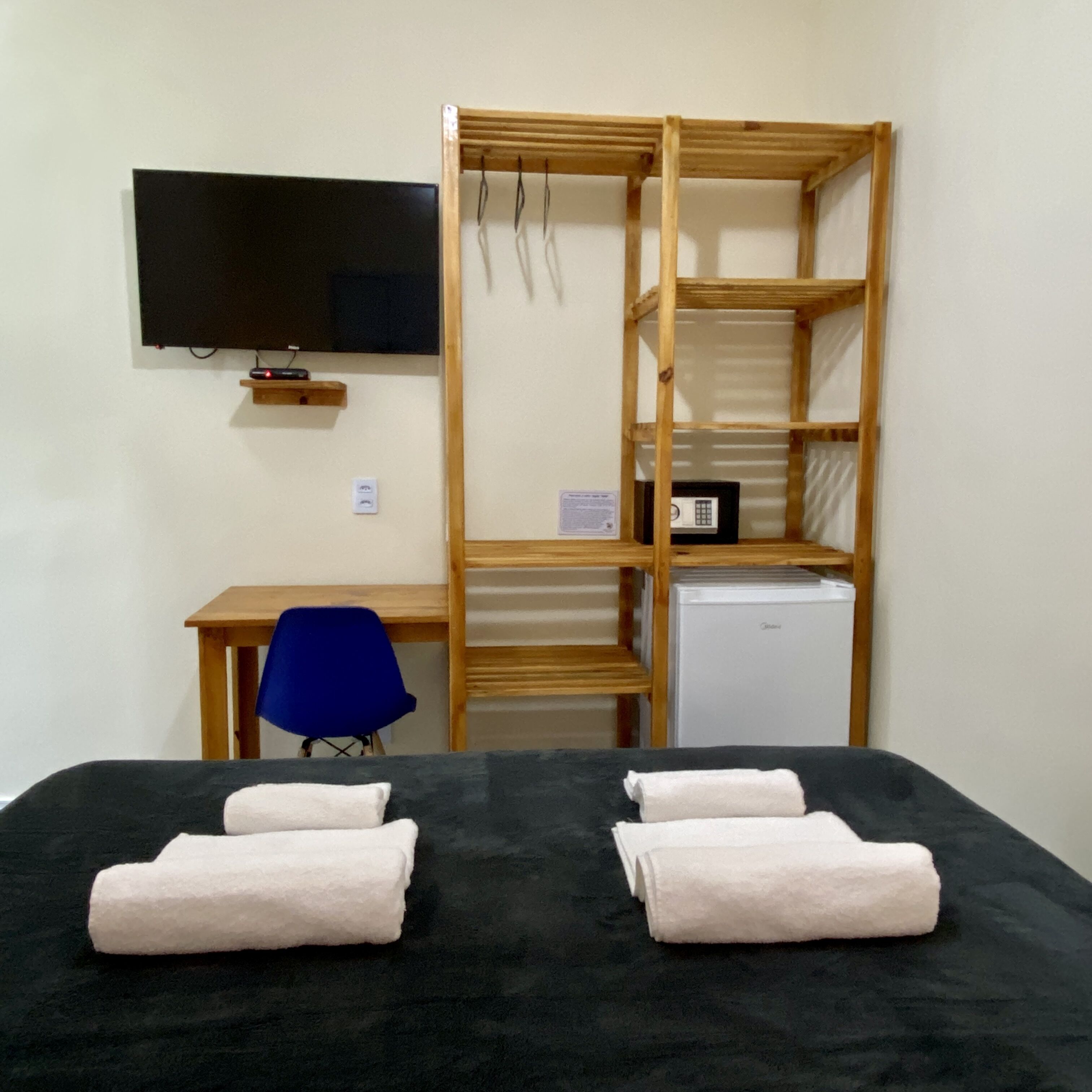 Een kamer met een bed, een bureau, een stoel, een televisie en een kleine koelkast.
