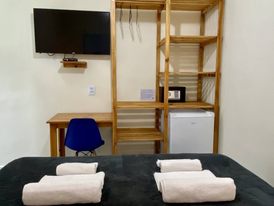 Ein Zimmer mit einem Bett, einem Schreibtisch, einem Stuhl, einem Fernseher und einem kleinen Kühlschrank.