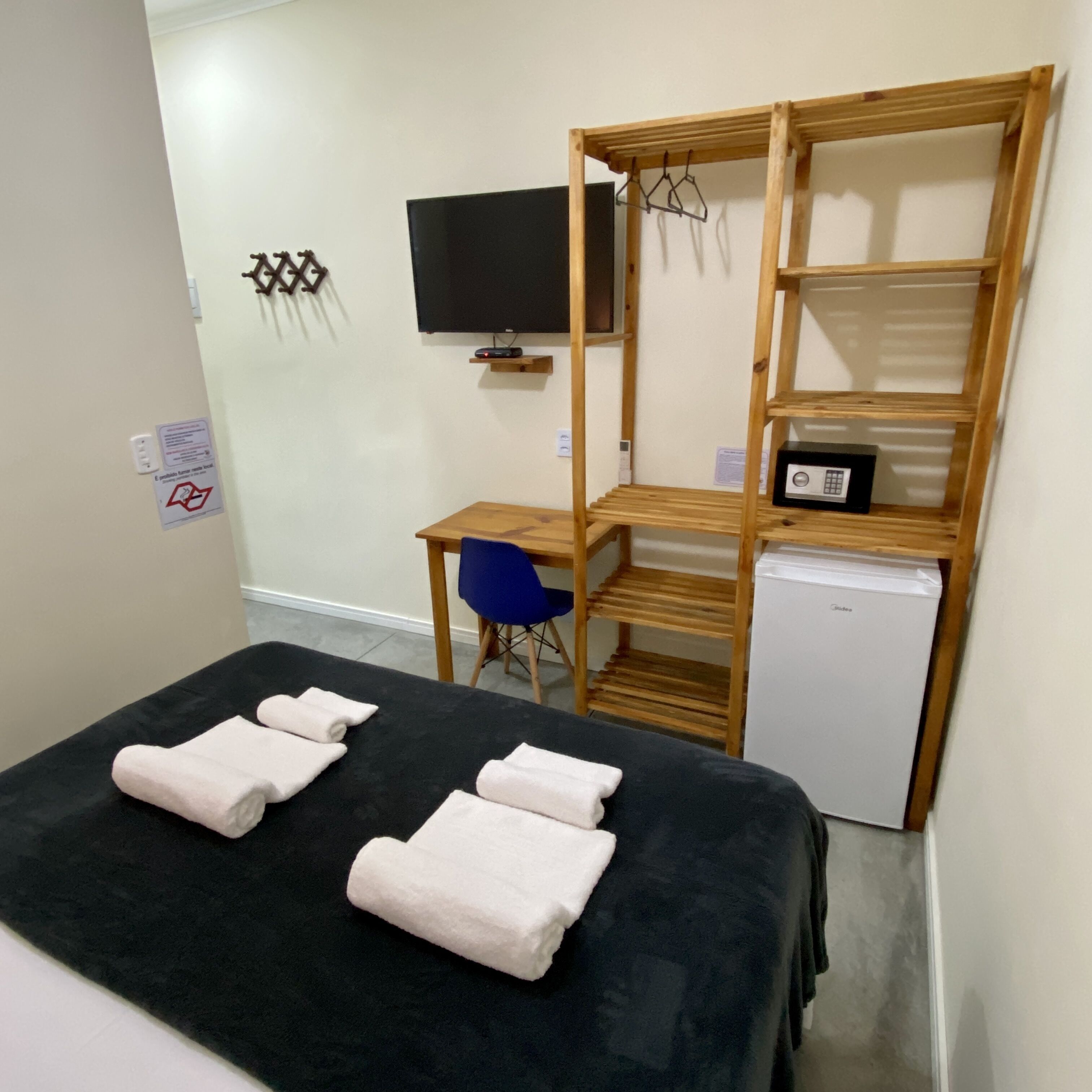 Una habitación pequeña con cama, escritorio, silla, televisión y refrigerador pequeño.