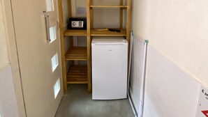 Una habitación compacta con estantería de madera empotrada, un refrigerador blanco y una radio pequeña.