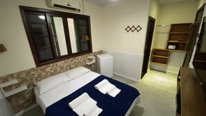 Una habitación de hotel con una cama, un espejo, un aire acondicionado blanco y un pequeño armario blanco.