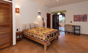 A bedroom with a wooden bed, a desk, and a chair, a balcony, and a painting on the wall.