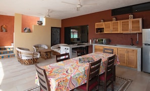 A dining area with a colorful tablecloth, wooden chairs, and a kitchen area with cabinets and a microwave. - WATERFRONT COLONIAL PENTHOUSE 112m2 COMPLETE FLOOR &INFINITY POOL (Barra de Navidad)