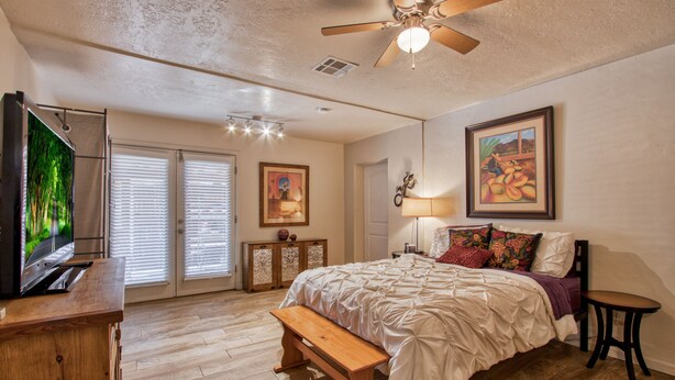 A bedroom with a bed, a bench, a TV, and a ceiling fan. - Adorable 2 BR at the heart of town! (Las Cruces)