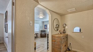 A hallway with a wooden floor, a wooden cabinet, and a mirror on the wall. - Adorable 2 BR at the heart of town! (Las Cruces)