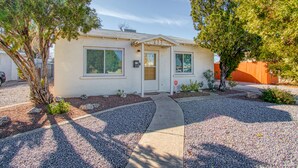 A single-story house with a front door, two windows with shutters, a small porch, and a gravel driveway. - Adorable 2 BR at the heart of town! (Las Cruces)