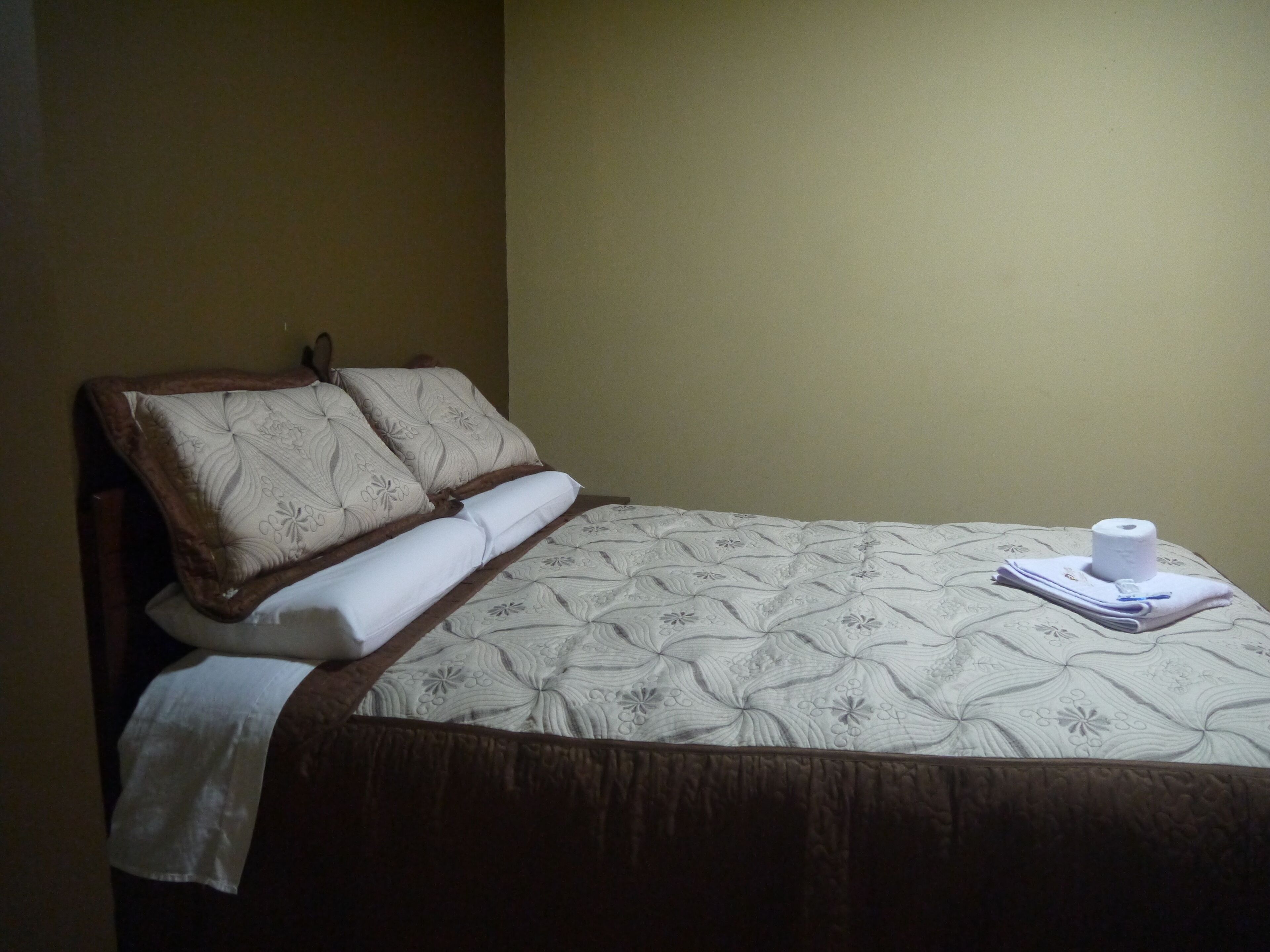 A neatly made bed with a floral-patterned bedspread, a wooden headboard, and a white towel folded at the foot of the bed.