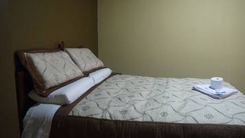 A neatly made bed with a floral-patterned bedspread, a wooden headboard, and a white towel folded at the foot of the bed.