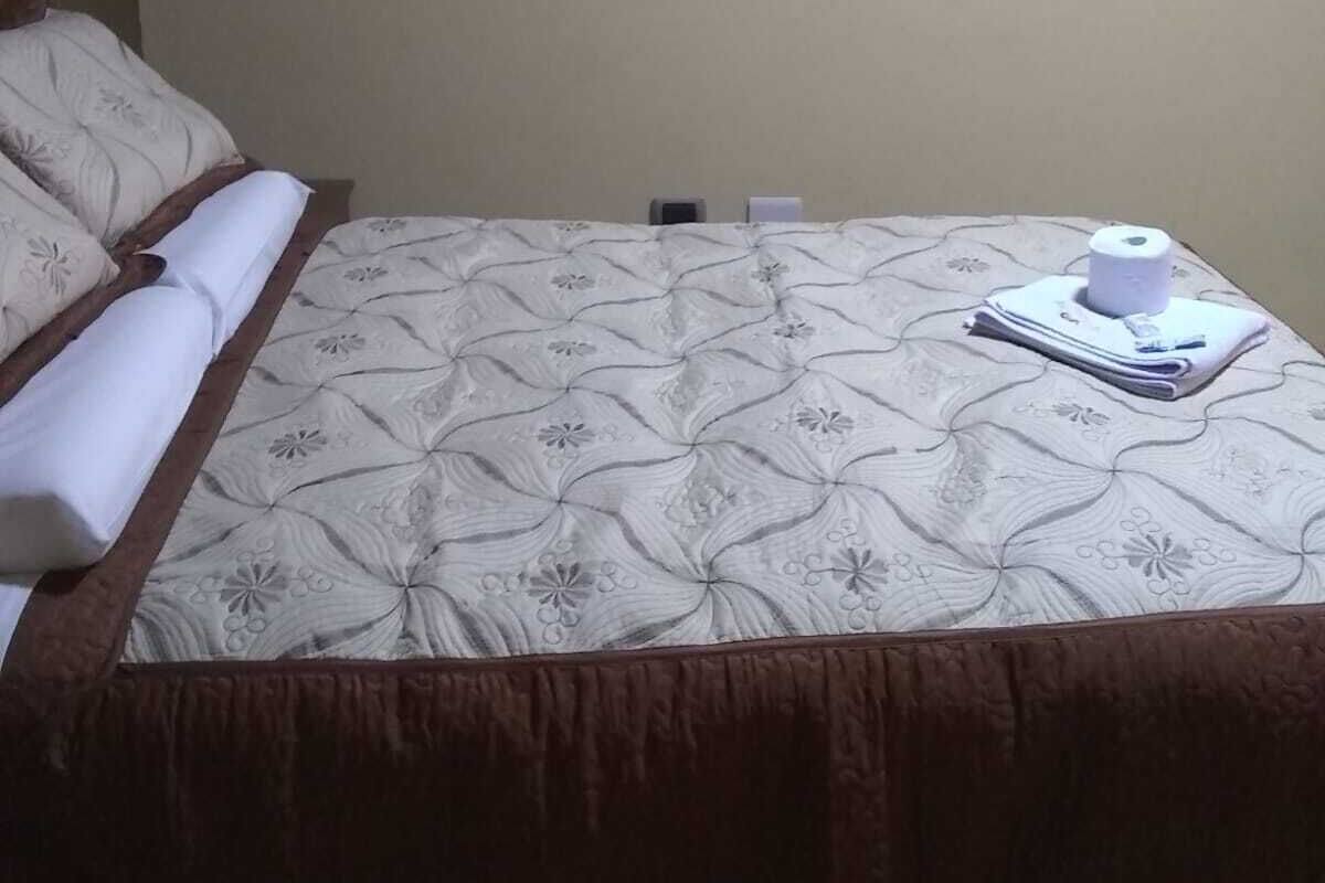 Una cama bien hecha con una colcha de estampado floral, una almohada y una toalla enrollada sobre la cama.