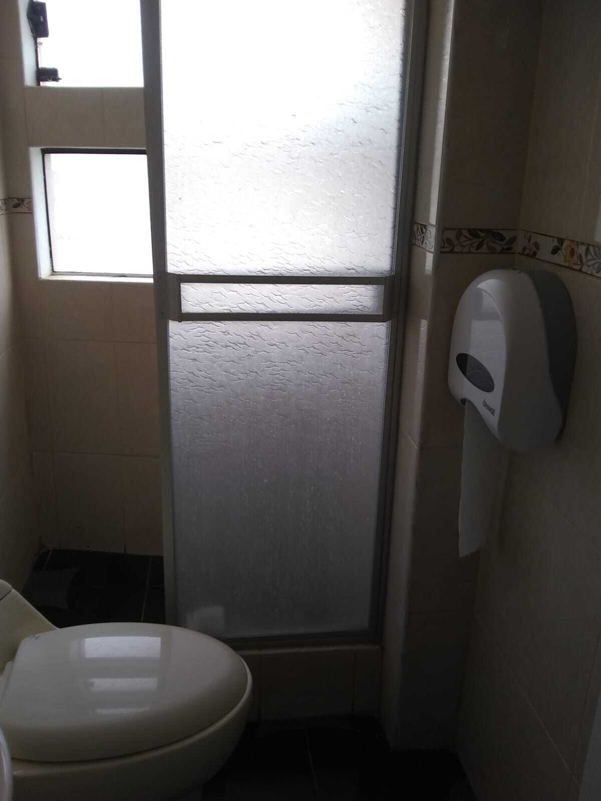 A small bathroom with a toilet, a hand dryer, and a frosted glass door.